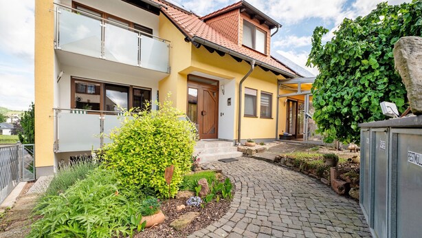 A two-story house with a yellow facade, a tiled roof, and a paved driveway.