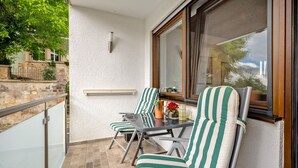 A balcony with two striped chairs, a small table, and a window with a view of a building and trees.