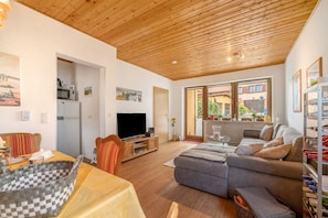 Un salon moderne avec un plafond en bois, un téléviseur, un canapé et un coin repas comprenant une table et des chaises.
