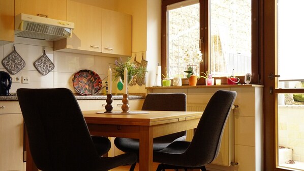A kitchen with a dining table, chairs, a window with plants, and a view of the outside.
