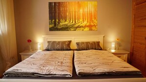 Un lit double avec une couvre-lit à motifs de forêt, une tête de lit blanche et un tableau représentant une forêt au-dessus du lit.