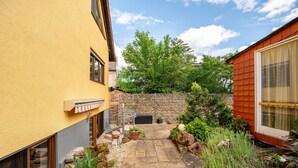 Une cour avec un chemin en pierre, des plantes en pot et un petit espace aménagé pour s’asseoir.