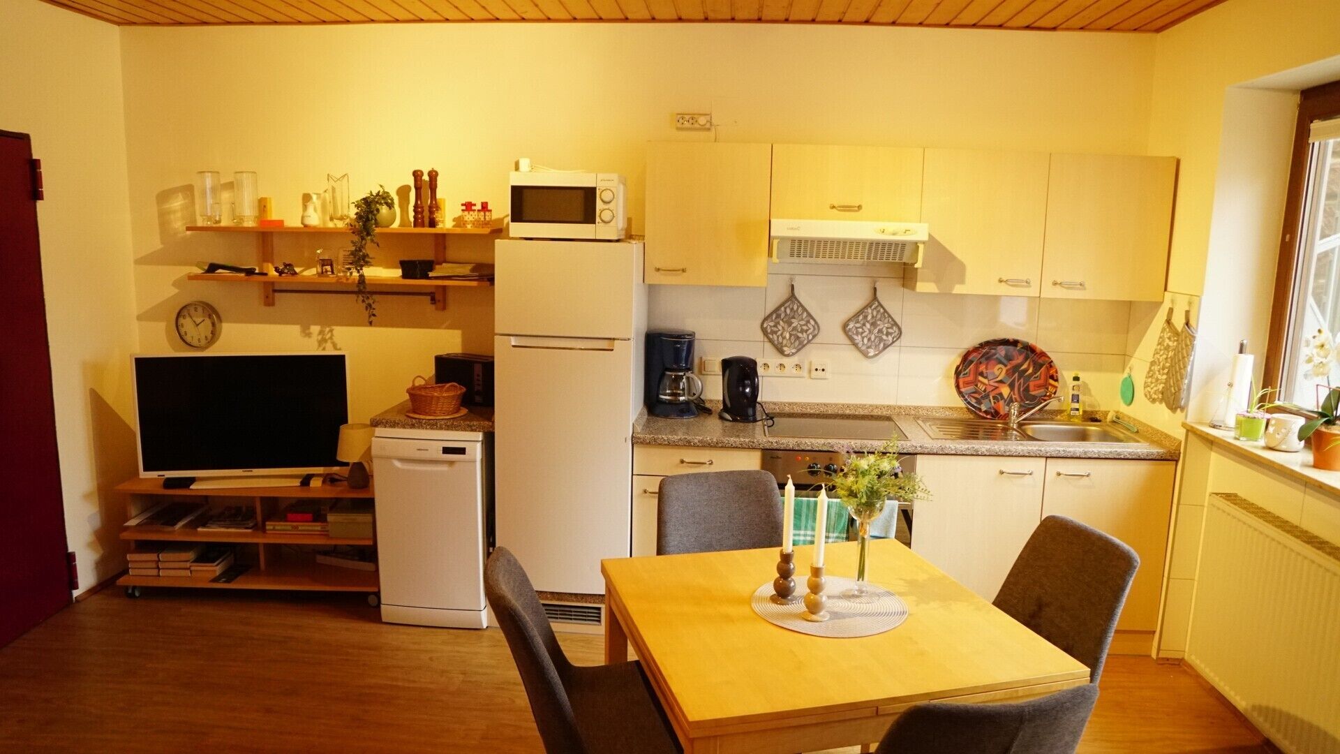 Una cocina compacta equipada con microondas, cafetera y un refrigerador pequeño. Cuenta con una mesa de comedor con sillas y un televisor sobre un mueble.