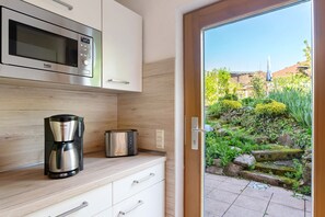 Eine Küche mit Mikrowelle, Kaffeemaschine und Toaster, einer Schiebetür zu einem Garten und einer Holzarbeitsplatte.