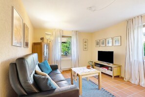 Ein Wohnzimmer mit einer Couch, einem Fernseher, einem Tisch und einem Fenster mit Vorhängen.