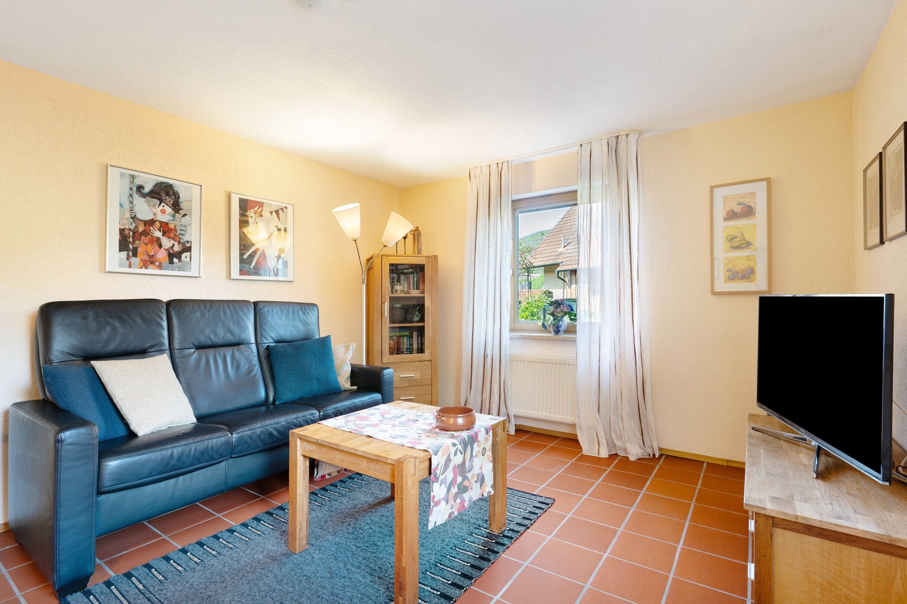 A living room with a sofa, a table with a bowl, a bookshelf, a TV, and a window with curtains.