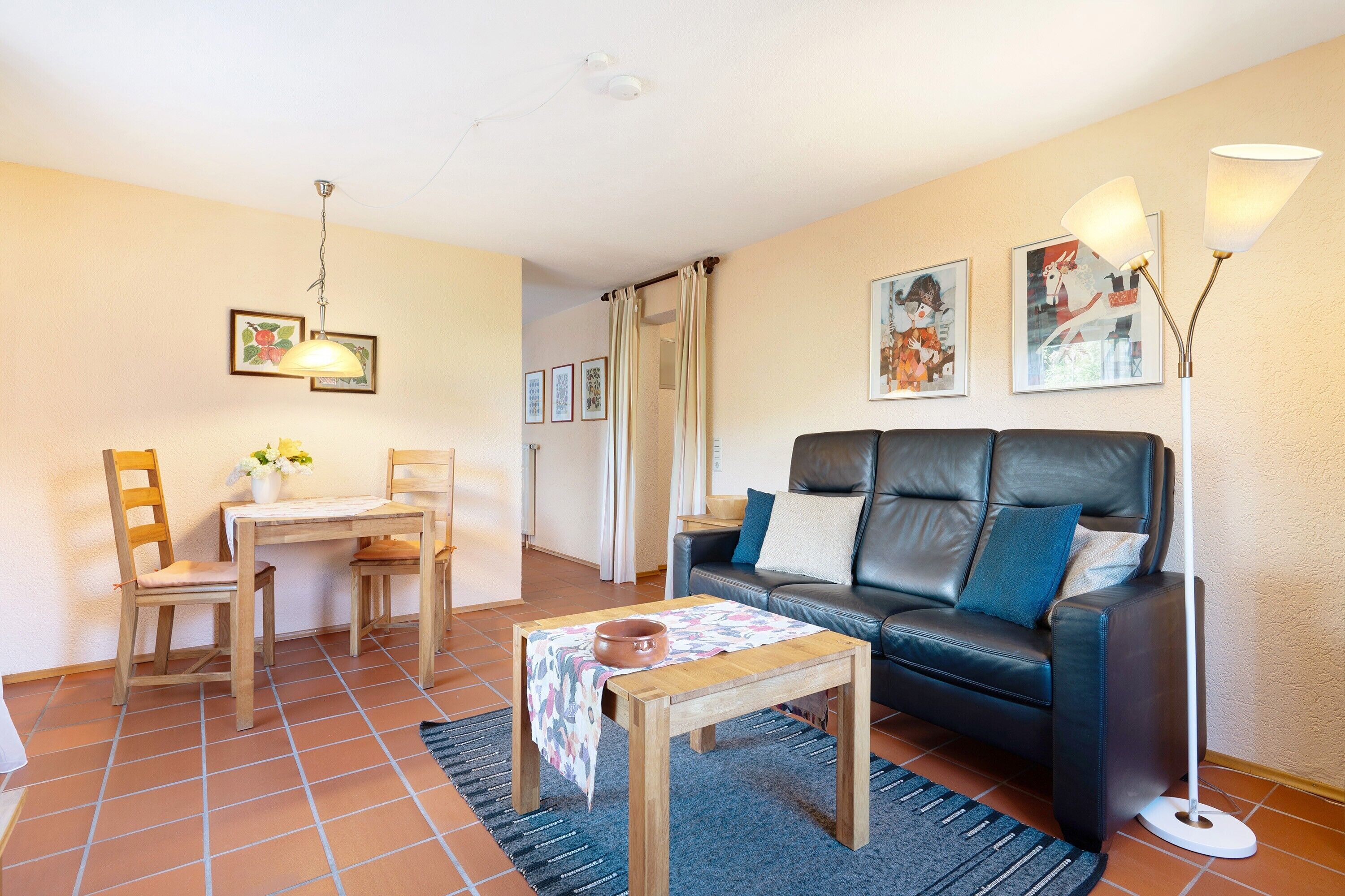 A living room with a sofa, a coffee table, a dining table, chairs, a lamp, and artwork on the walls.