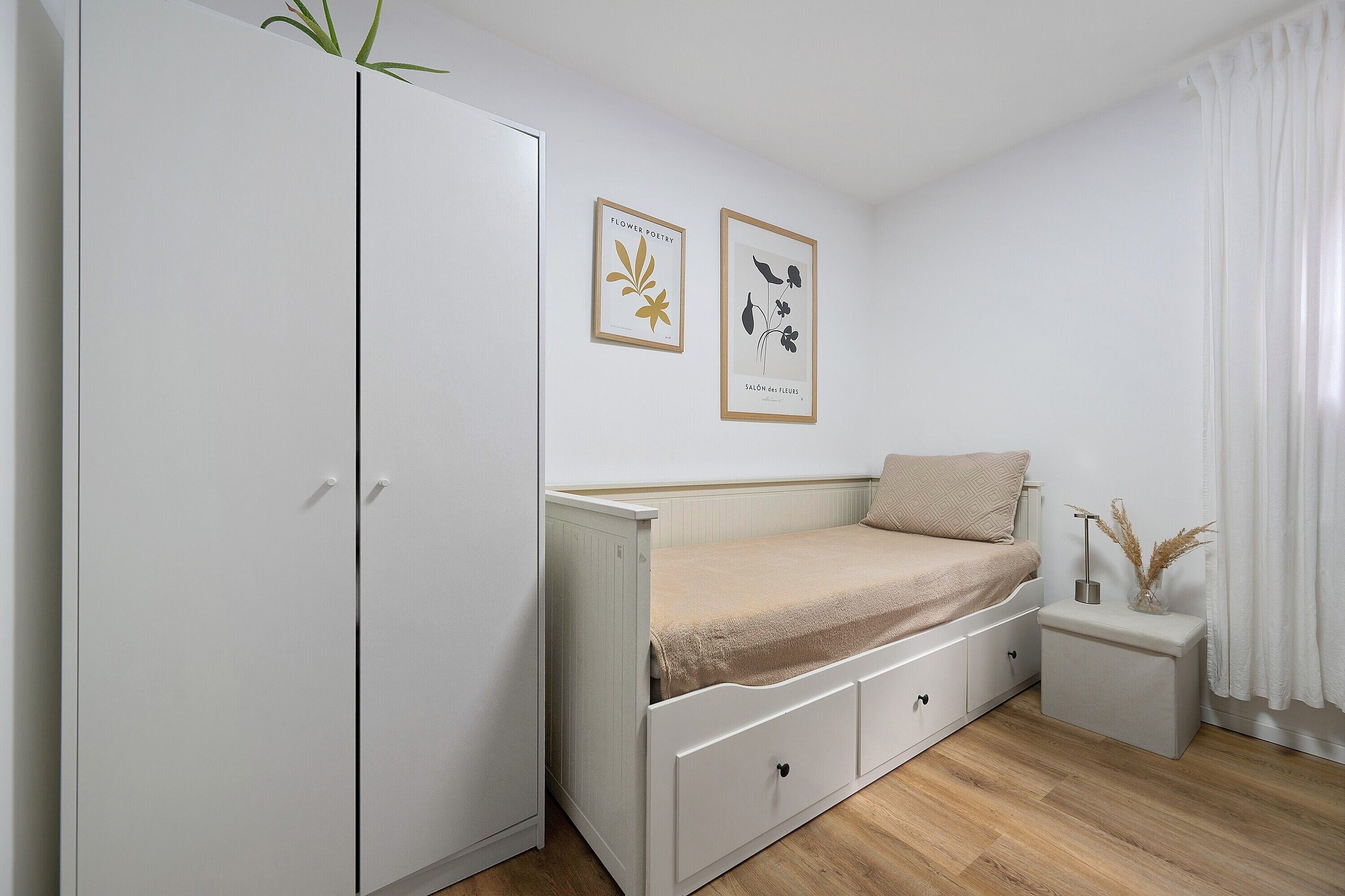 A bedroom with a bed, a wardrobe, a bedside table, and two framed pictures on the wall.
