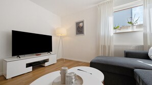 A modern living room with a flat-screen TV, a white console table, a round coffee table with candles, a grey sofa, and a window with potted plants. - Apartment “Auszeit” with Wi-Fi – newly renovated, family-friendly, central location (Calw)