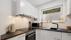 A modern kitchen with white cabinets, a black countertop, a built-in oven, a microwave, and a window with a view of greenery. - Apartment “Auszeit” with Wi-Fi – newly renovated, family-friendly, central location (Calw)