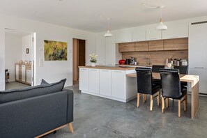 Une cuisine moderne avec des meubles blancs, un îlot central en bois et un coin repas comprenant une table et des chaises.