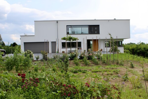 A modern two-story house with a garage, surrounded by a garden with various plants and flowers. - Apartment 'Ferienwohnung Im Obstgarten' with Private Terrace and Wi-Fi (Ihringen)