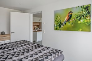 Une chambre à coucher avec une couvre-lit à motifs, une porte donnant sur la cuisine et un tableau représentant des oiseaux accroché au mur.