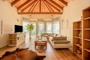 Un salón amplio con techo de madera alta, televisión, sofá, mesa de centro y estantería.