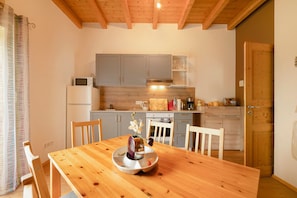 A wooden dining table with chairs, a kitchen with grey cabinets, a microwave, and a coffee maker.