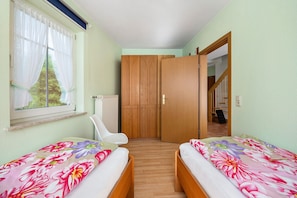 A bedroom with two beds, a window with curtains, a radiator, and a wooden wardrobe.