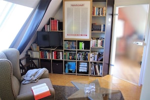 A room with a bookshelf, a television, a sofa, and a glass table with glasses.