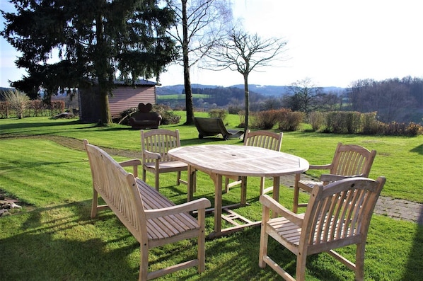 A wooden outdoor seating area with a table and chairs, surrounded by a well-maintained lawn and trees.