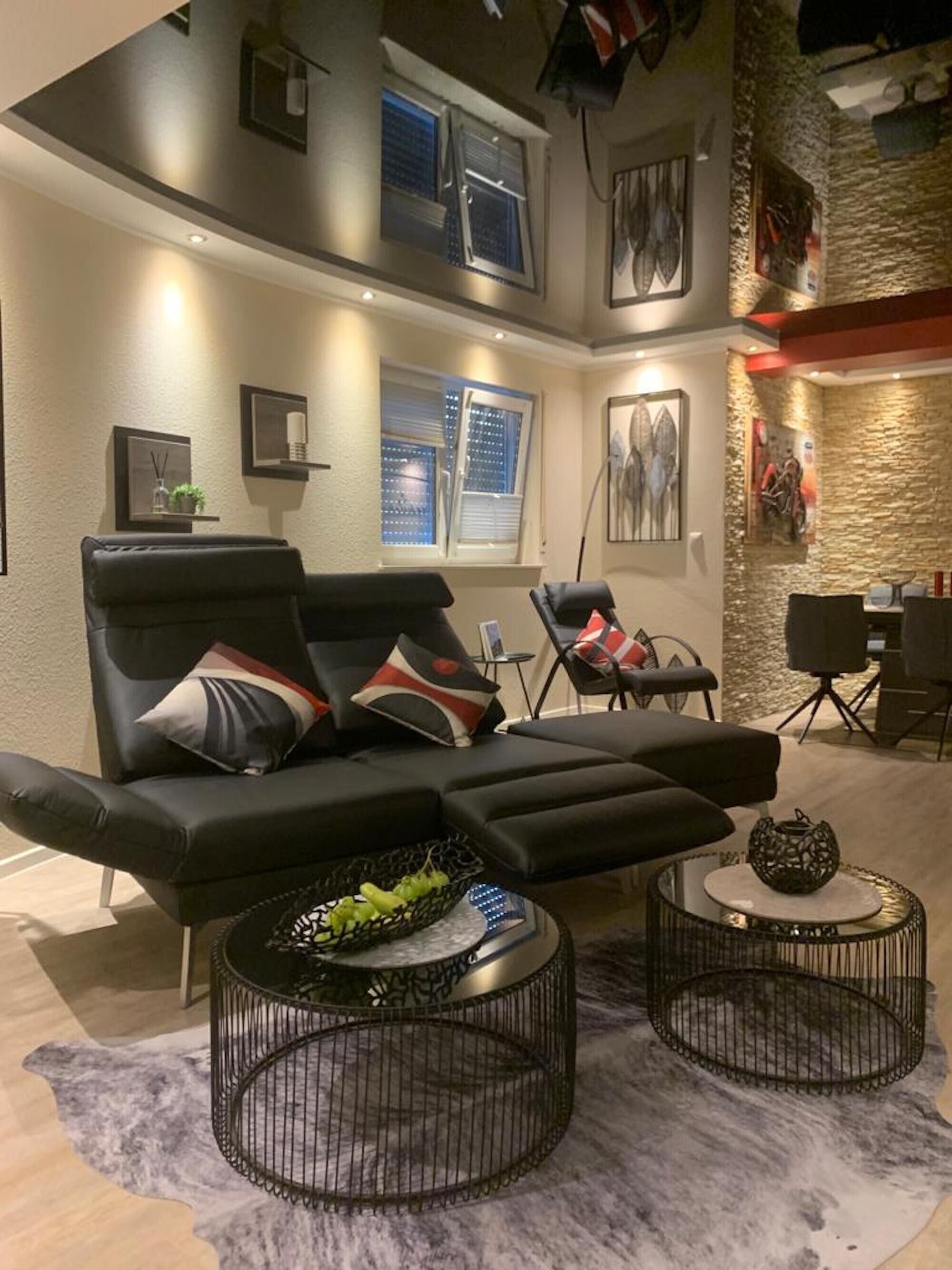 Ein modernes Wohnzimmer mit einer schwarzen Couch, zwei runden Couchtischen und einer Wand mit Steinverkleidung.