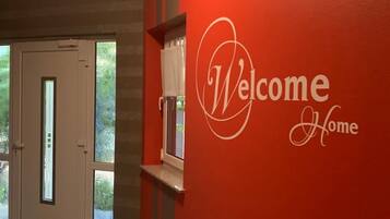 Ein Gang mit roter Wand und einem 'Welcome Home' Schild.
