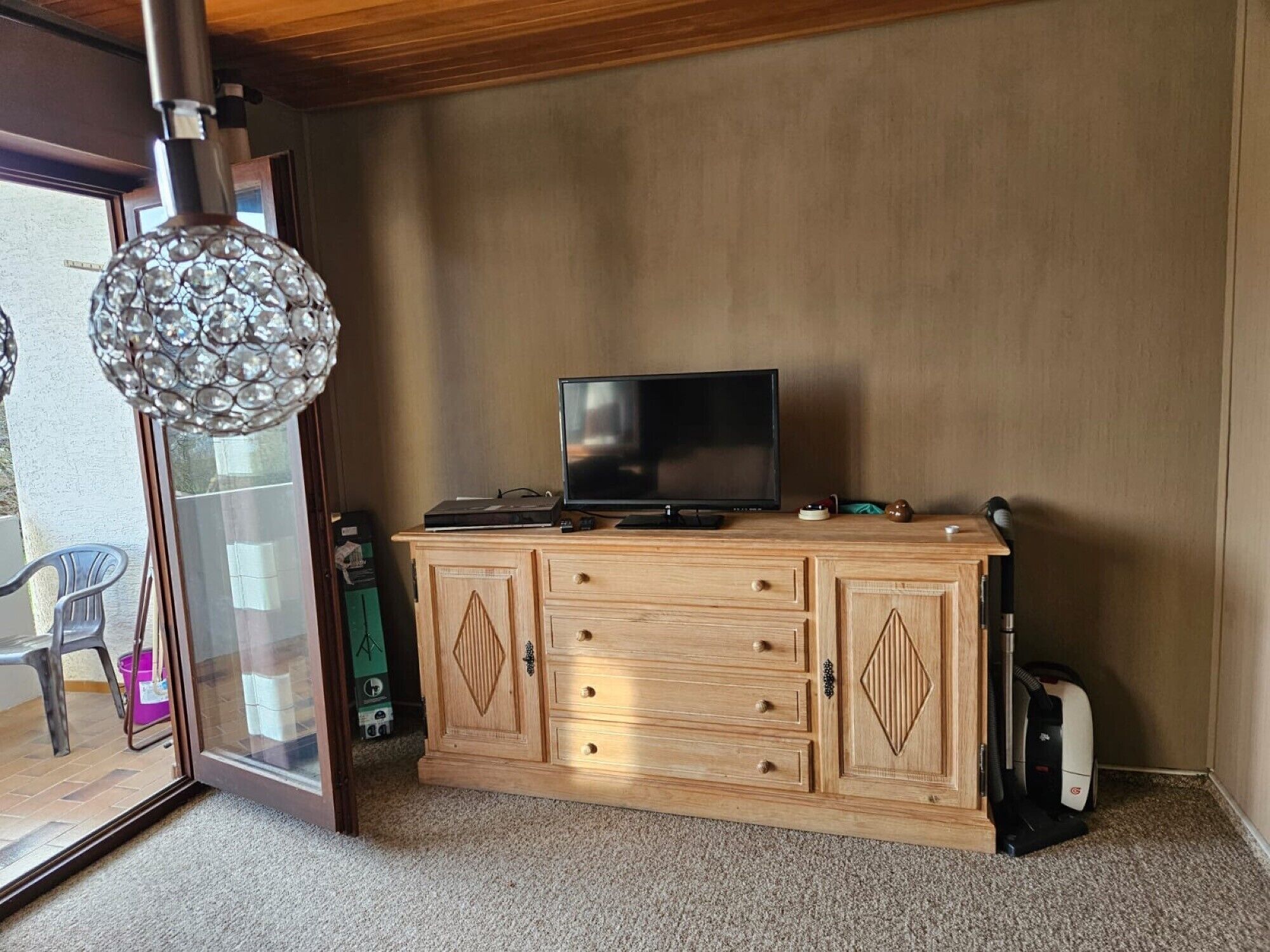 A room with a wooden cabinet, a television, and a vacuum cleaner.