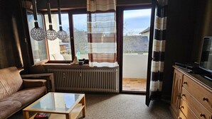 Una sala de estar con sofá, mesa de centro, televisor y vista a través de una puerta corrediza de vidrio.