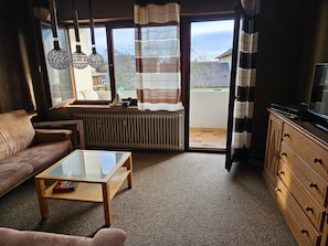 A living room with a sofa, coffee table, TV, and a view through a sliding glass door.