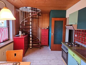 A kitchen with a spiral staircase, a red cabinet, a stove, and a window with a butterfly decoration.