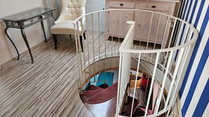 Una habitación con una escalera de caracol, una mesa de cristal, una butaca acolchada y un armario de madera.