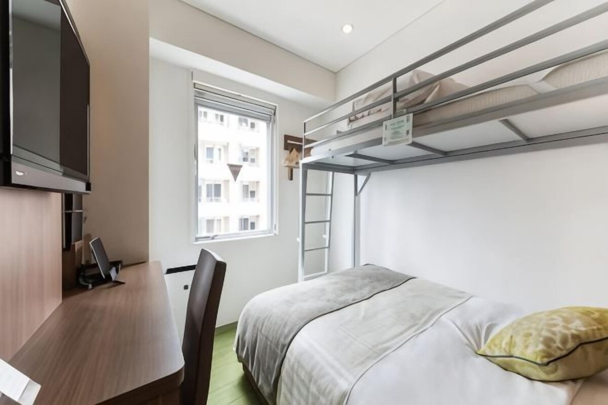 Une petite pièce avec un lit superposé, un bureau et une fenêtre.