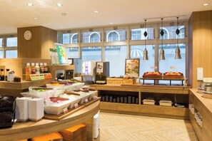 Un espace buffet proposant divers plats, une horloge au mur et une grande fenêtre donnant sur l’extérieur.
