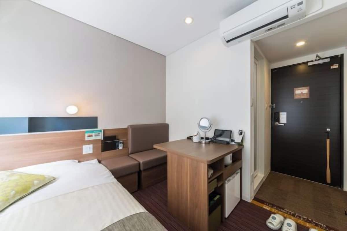 Une chambre d’hôtel comprenant un lit, un bureau, une chaise, une petite table, un miroir et une porte.