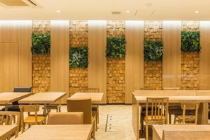 A hotel dining area with wooden tables and chairs, a stone wall with greenery, and a wooden door. - Super Hotel Premier Hakataeki (Fukuoka)