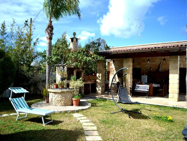 Un patio con una silla de lounge, una mecedora y una jardinera de piedra con plantas en macetas.