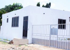 Un bâtiment blanc avec une entrée fermée par un portail, une porte et des fenêtres.