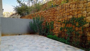 A tiled patio area with a stone wall and greenery.
