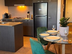 A modern kitchen with a built-in island, stainless steel appliances, and a dining area with a glass table and green chairs. - Ideal, Quiet 1BR Prahran Apt Near Cafes, Transport (Prahran)