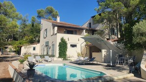 A two-story house with a swimming pool, outdoor seating, and a pergola.