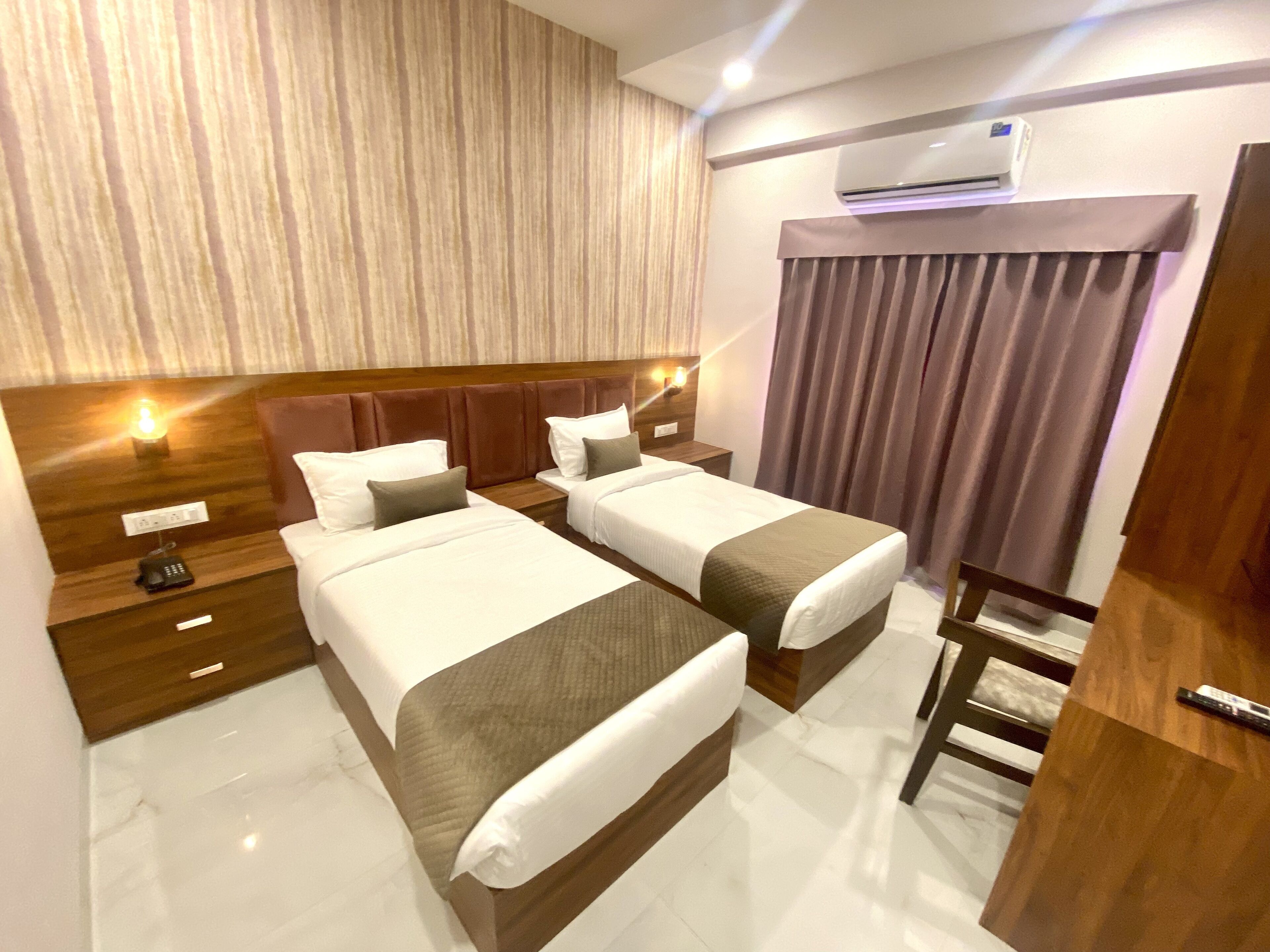 A hotel room with two beds, a wooden headboard, a nightstand with a phone, and an air conditioning unit on the wall.