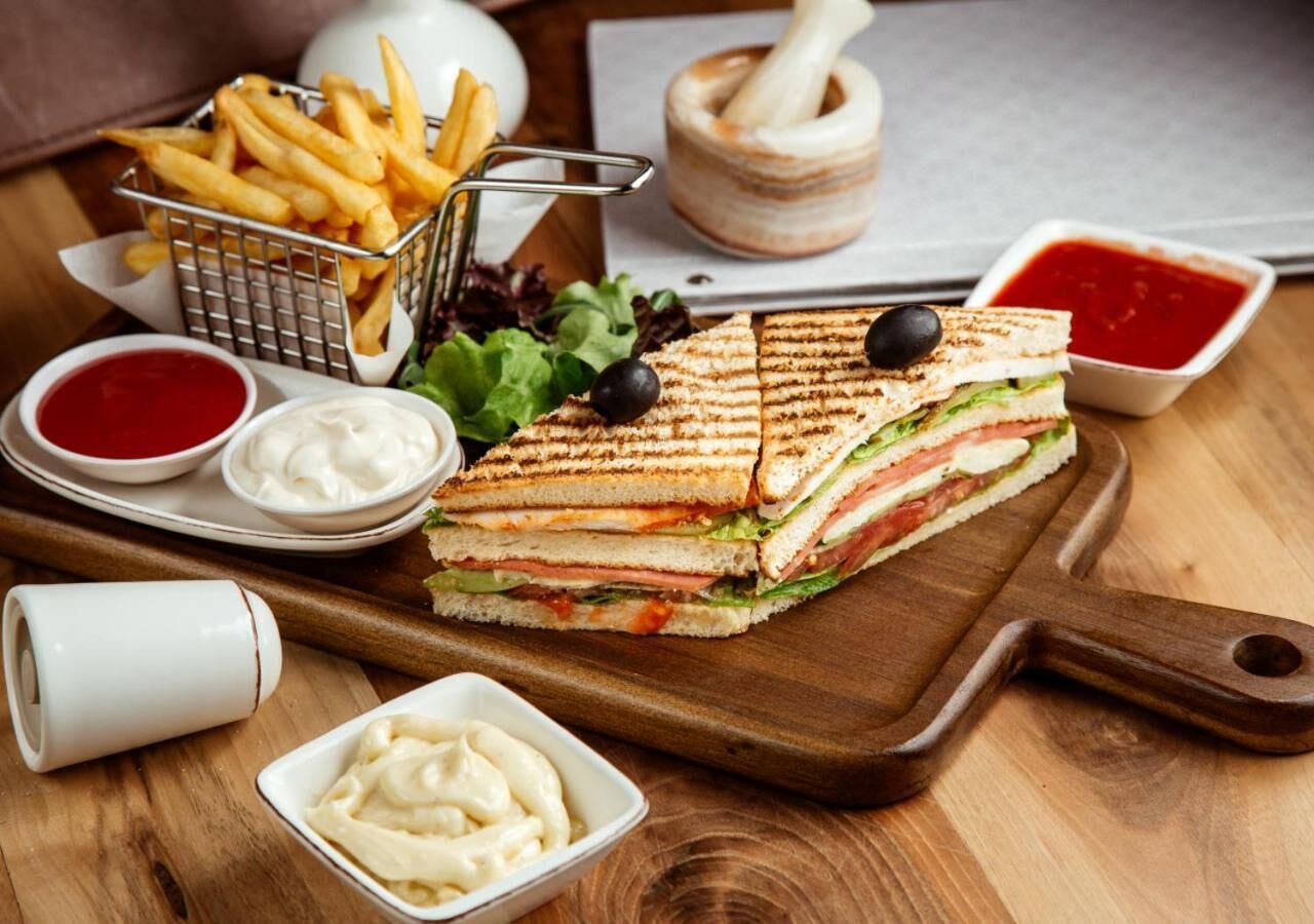 A sandwich on a wooden board, accompanied by French fries, salad, and condiments.