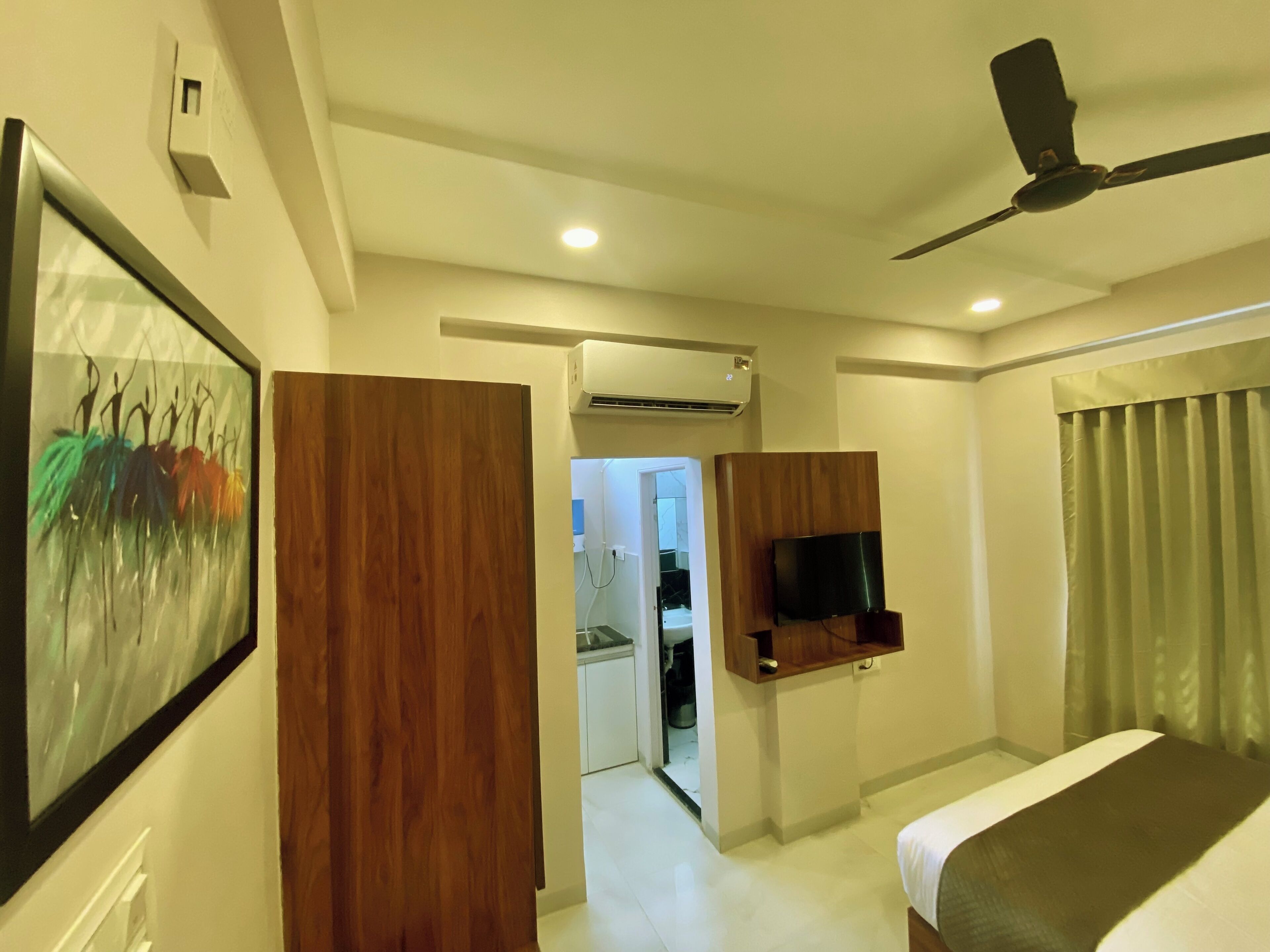 A hotel room with a bed, a ceiling fan, a mounted TV, and a door leading to a bathroom.