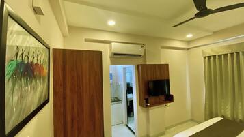 A hotel room with a bed, a ceiling fan, a mounted TV, and a door leading to a bathroom.