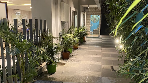 Un espace d’accueil avec un panneau lumineux au néon, des plantes en pot et un sol carrelé.
