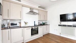 Une cuisine moderne avec des meubles blancs, un four à micro-ondes encastré, un four traditionnel et un grand téléviseur à écran plat fixé au mur.