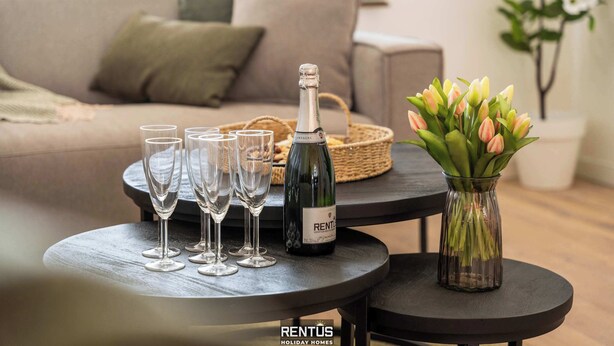 A living room with a sofa, a coffee table with a bottle of champagne and glasses, and a vase with flowers. - Casa Diva – renovated house for 12 in Blankenberge (Blankenberge)