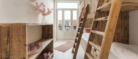 Una habitación pequeña con literas, estantes de madera y una alfombra pequeña.