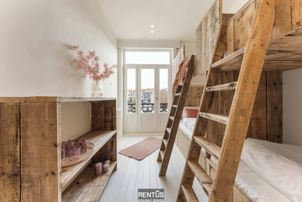 Une petite pièce avec un lit superposé, des étagères en bois et un petit tapis.