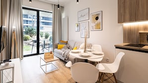 Un salon moderne avec un canapé, une table à manger et des chaises. On y trouve également un téléviseur, une table basse et une fenêtre avec des rideaux.