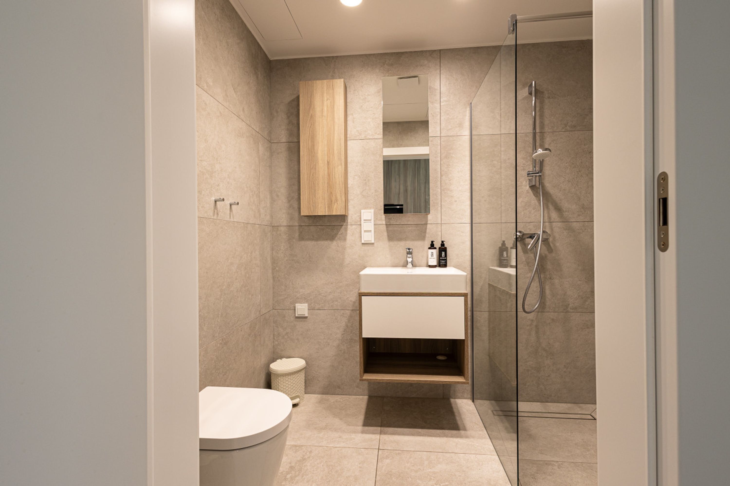 Un baño moderno con cabina de ducha de vidrio, inodoro y tocador con espejo y espacio de almacenamiento.