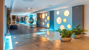 A modern lobby with a reflective floor, hanging chairs, and circular wall lights.